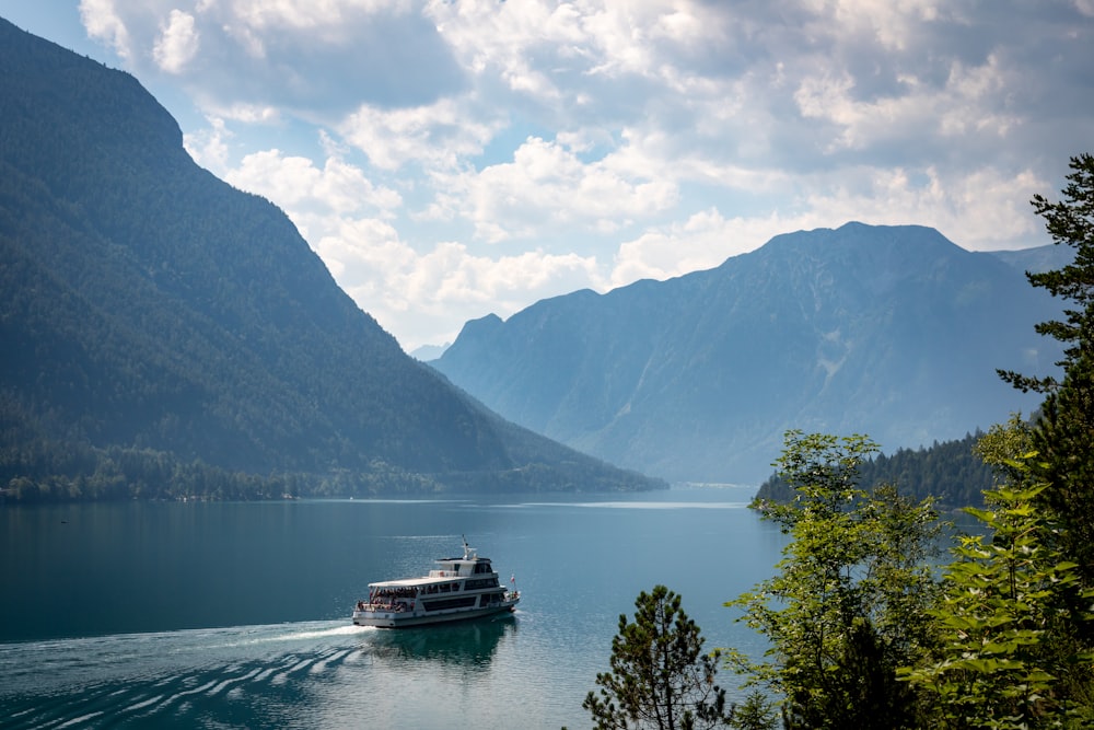 white boat on body of water near green trees and mountain during daytime