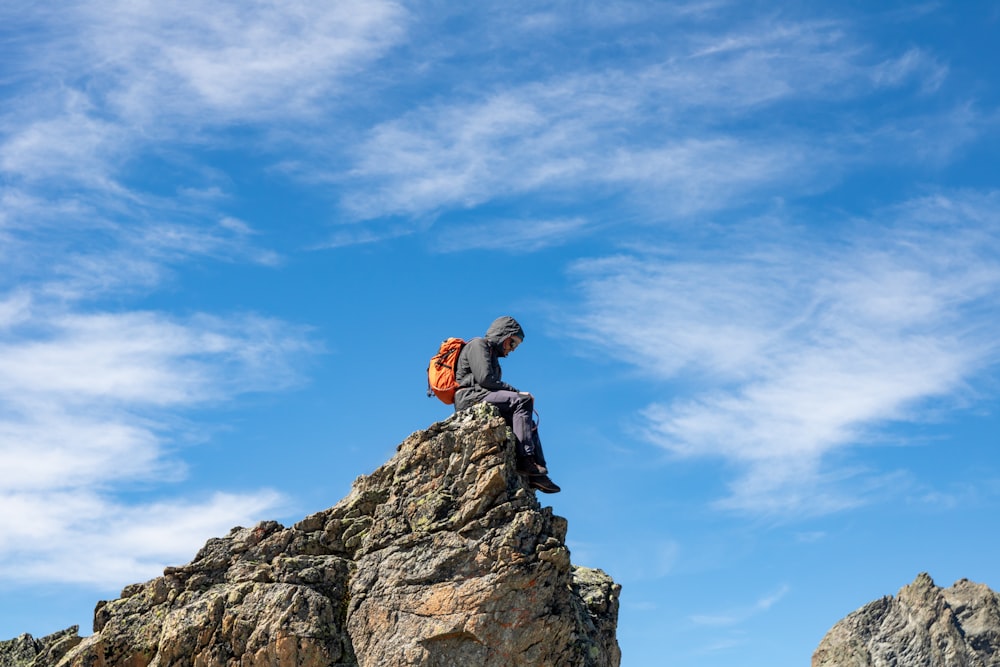 uomo che si siede sulla roccia sotto il cielo blu durante il giorno