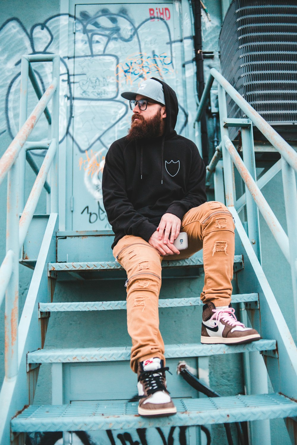 man in black hoodie and brown pants sitting on white metal staircase