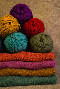 Handmade colorful dog sweaters displayed on a cozy wooden table with vibrant yarn balls.