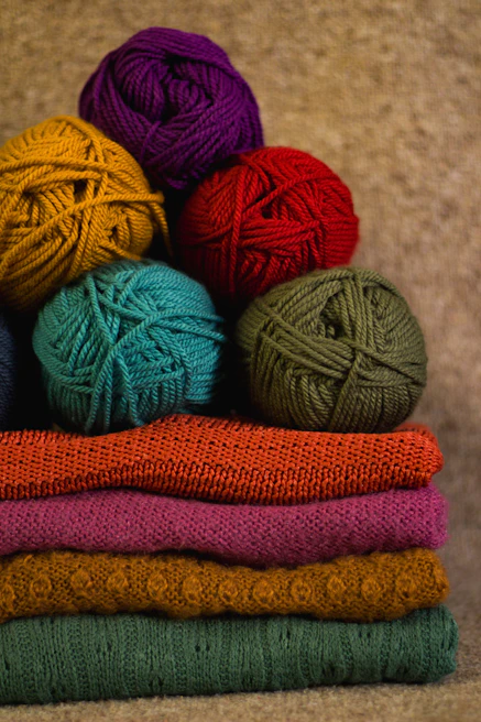 Soft hand knitting yarn balls in warm tones neatly stacked with knitting needles