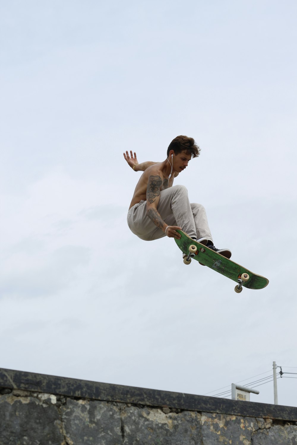 uomo in canotta bianca e pantaloni verdi che cavalcano lo skateboard verde durante il giorno