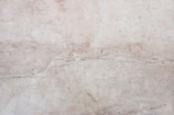 A close-up view of a light beige marble surface with natural veins and patterns, displaying subtle variations in tone and texture.