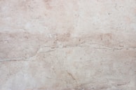 A close-up view of a light beige marble surface with natural veins and patterns, displaying subtle variations in tone and texture.