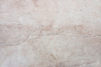 A close-up view of a light beige marble surface with natural veins and patterns, displaying subtle variations in tone and texture.