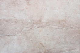 A close-up view of a light beige marble surface with natural veins and patterns, displaying subtle variations in tone and texture.