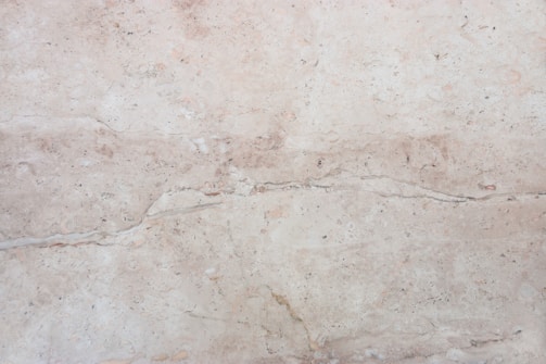 A close-up view of a light beige marble surface with natural veins and patterns, displaying subtle variations in tone and texture.