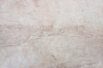 A close-up view of a light beige marble surface with natural veins and patterns, displaying subtle variations in tone and texture.