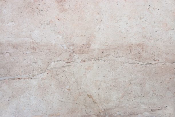 A close-up view of a light beige marble surface with natural veins and patterns, displaying subtle variations in tone and texture.