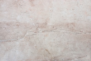A close-up view of a light beige marble surface with natural veins and patterns, displaying subtle variations in tone and texture.
