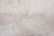 A close-up view of a light beige marble surface with natural veins and patterns, displaying subtle variations in tone and texture.