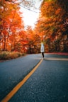 woman in white jacket and black pants standing on road between trees during daytime