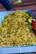 A large pile of golden-brown roasted or fried flakes is placed in an open tray. Next to the flakes, there are fresh green chilies, a lemon, and some red tomatoes.