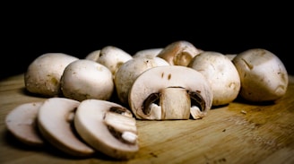 Several whole and sliced mushrooms are arranged on a wooden surface, with a dark background that highlights their texture and freshness.