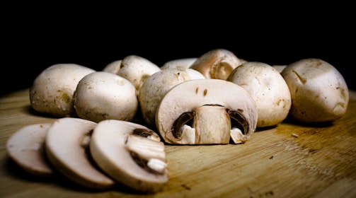 Several whole and sliced mushrooms are arranged on a wooden surface, with a dark background that highlights their texture and freshness.