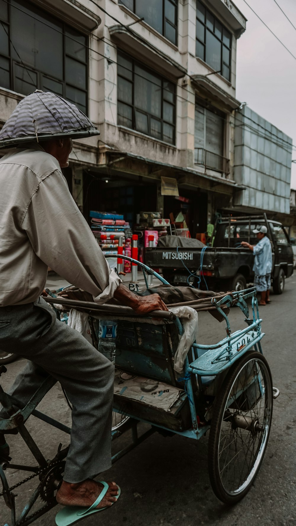 man in brown coat and brown hat riding on blue and red trike during daytime