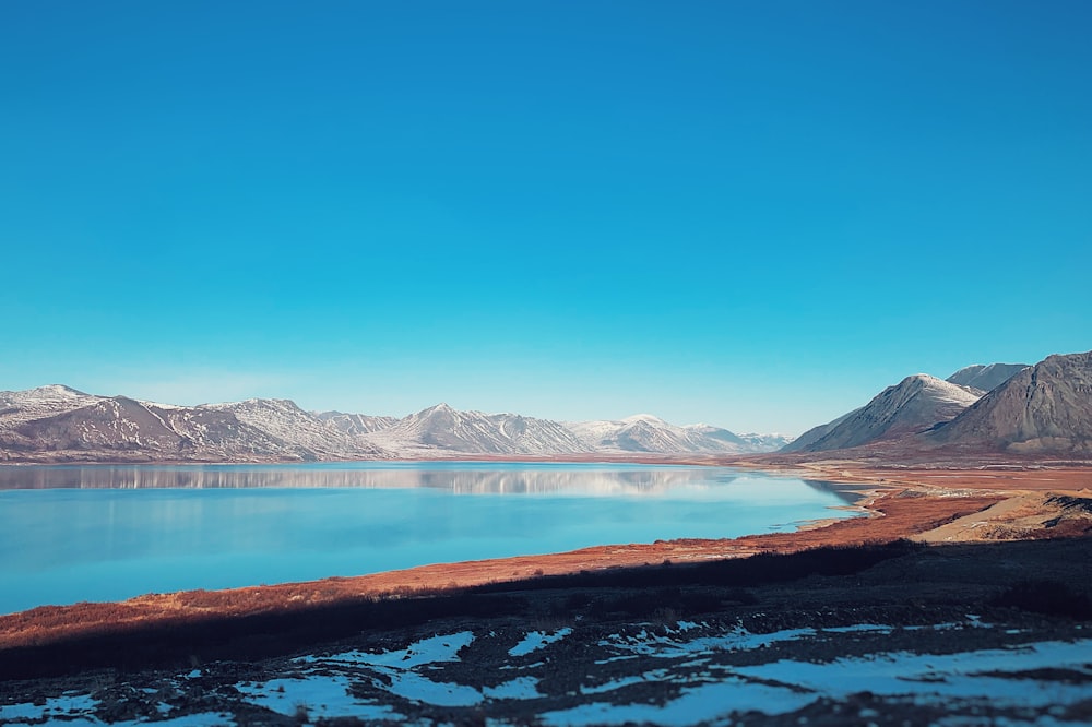 blue body of water near mountain under blue sky during daytime