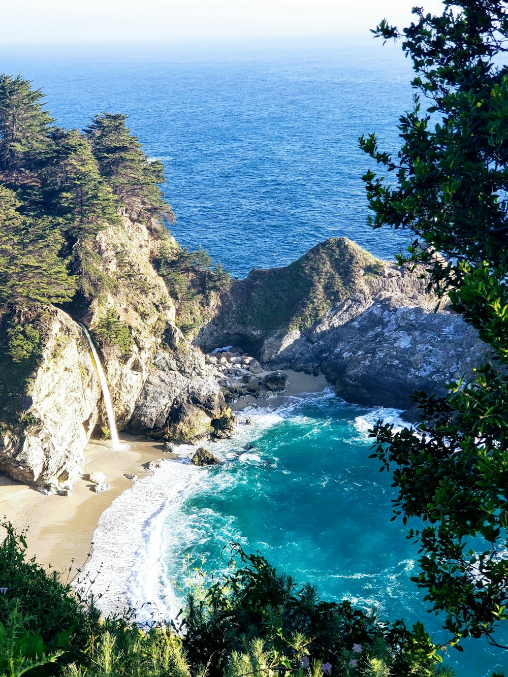 green trees on brown rocky mountain beside blue sea during daytime