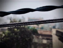 Close-up of wet, oily wires twisted around a rain-soaked industrial grate with blurred background.