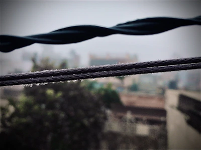 Close-up of wet, oily wires twisted around a rain-soaked industrial grate with blurred background.