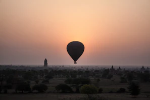 A golden hot air balloon drifting gracefully over the ancient Luxor temples at sunrise.