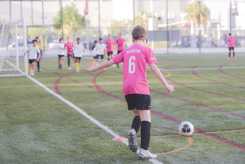 man in red and white soccer jersey kicking soccer ball during daytime