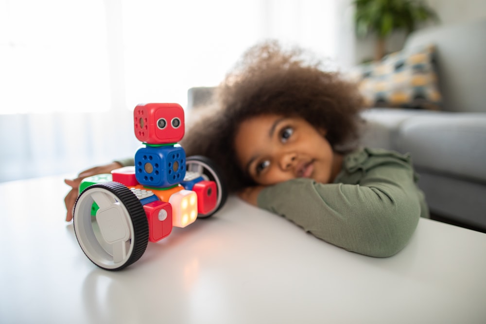 menino deitado na cama brincando com caminhão de brinquedo vermelho e azul