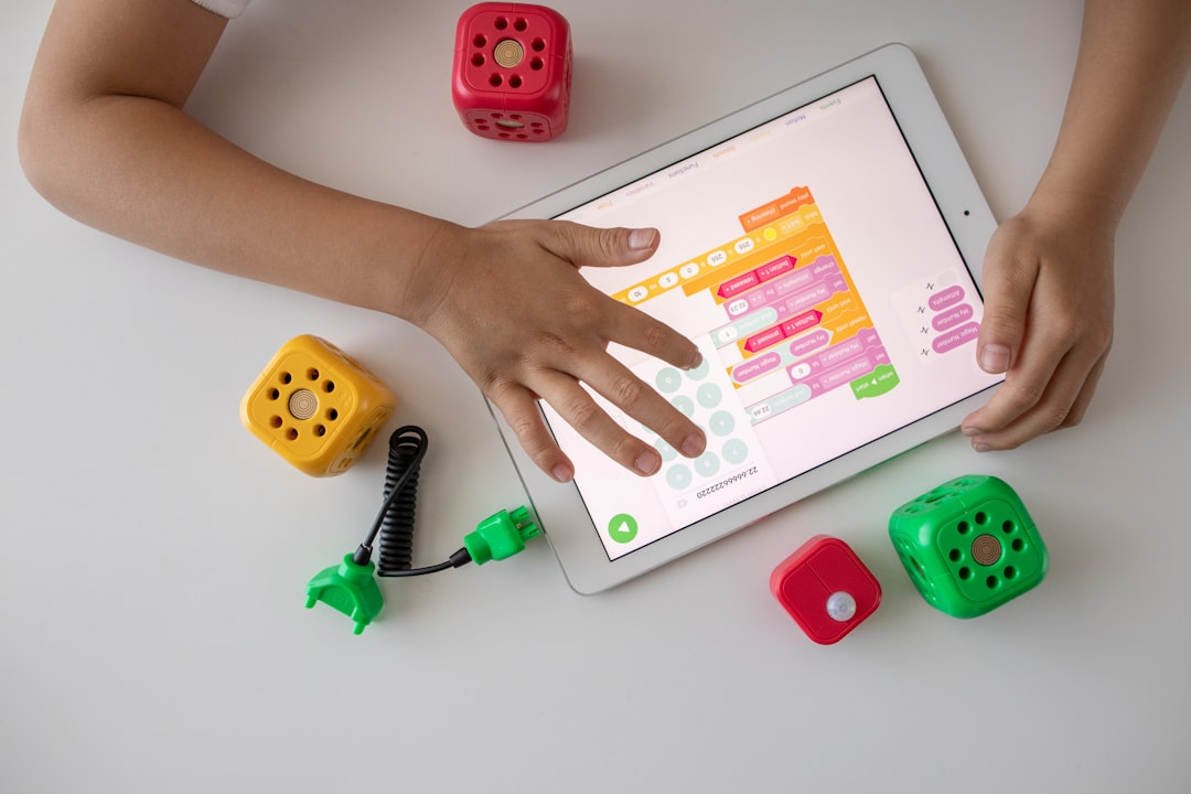 person holding white ipad on white table, Kid using a tablet for visual programming