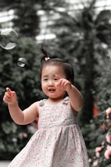 girl in pink and white floral sleeveless dress holding bubble during daytime