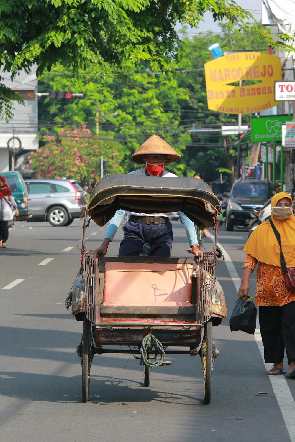 Mann in orangefarbenem Hemd und schwarzer Hose, der tagsüber einen braunen Holzwagen auf der Straße trägt