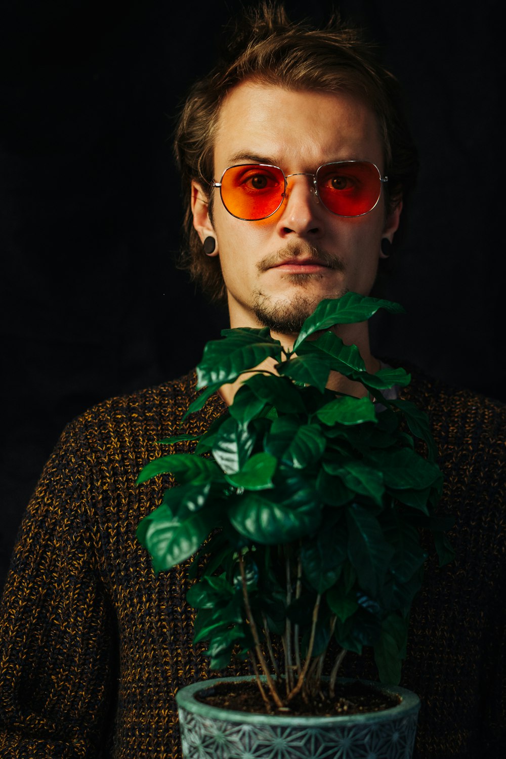 man in black and white long sleeve shirt wearing sunglasses standing beside green plant