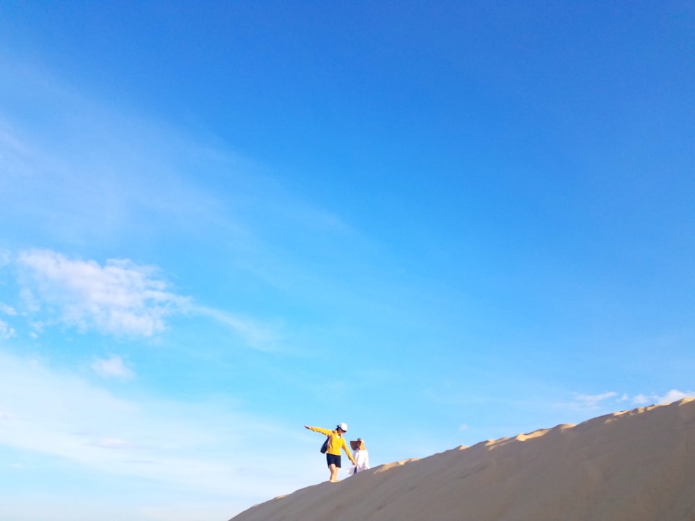 person in yellow jacket and black pants walking on brown sand under blue sky during daytime