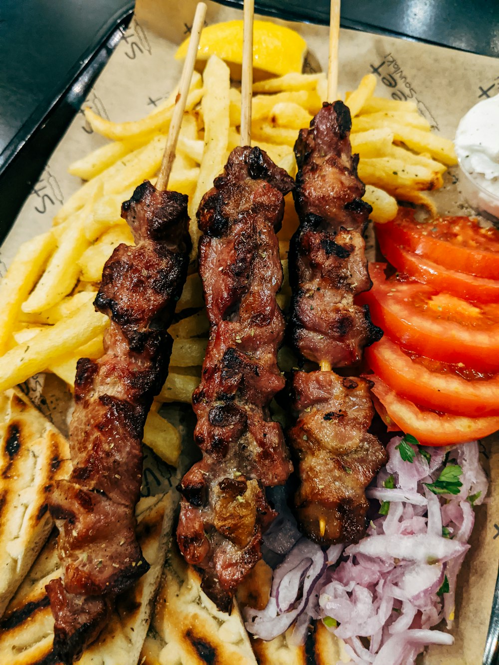 gegrilltes Fleisch mit Tomatenscheiben und grünem Gemüse auf weißem Keramikteller