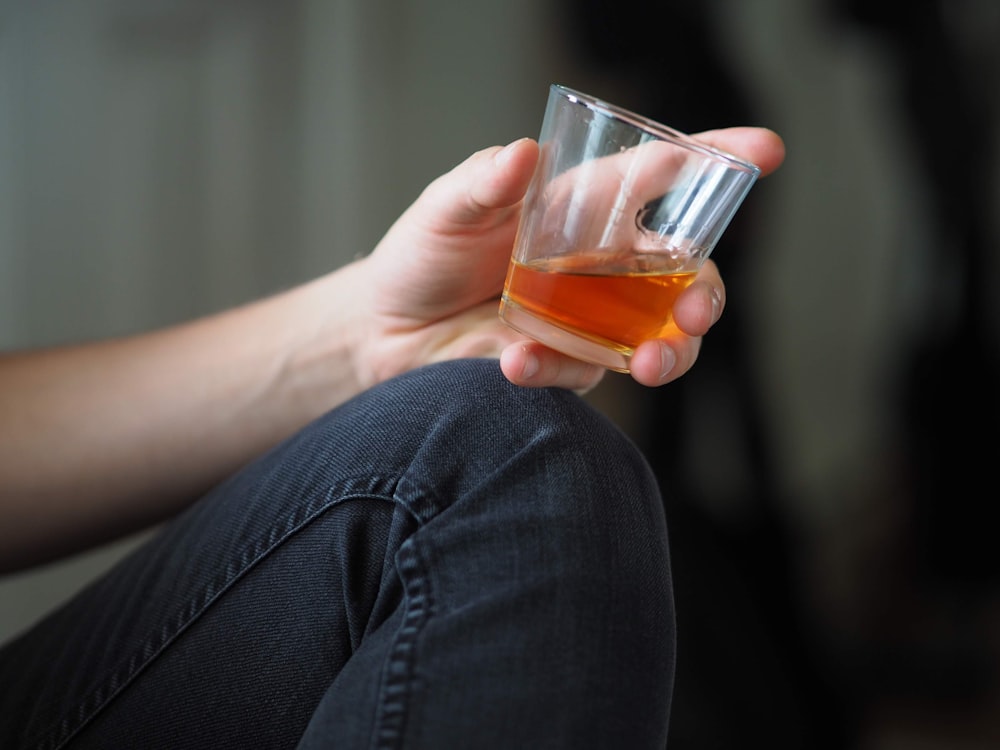 personne tenant un verre à boire transparent avec un liquide orange