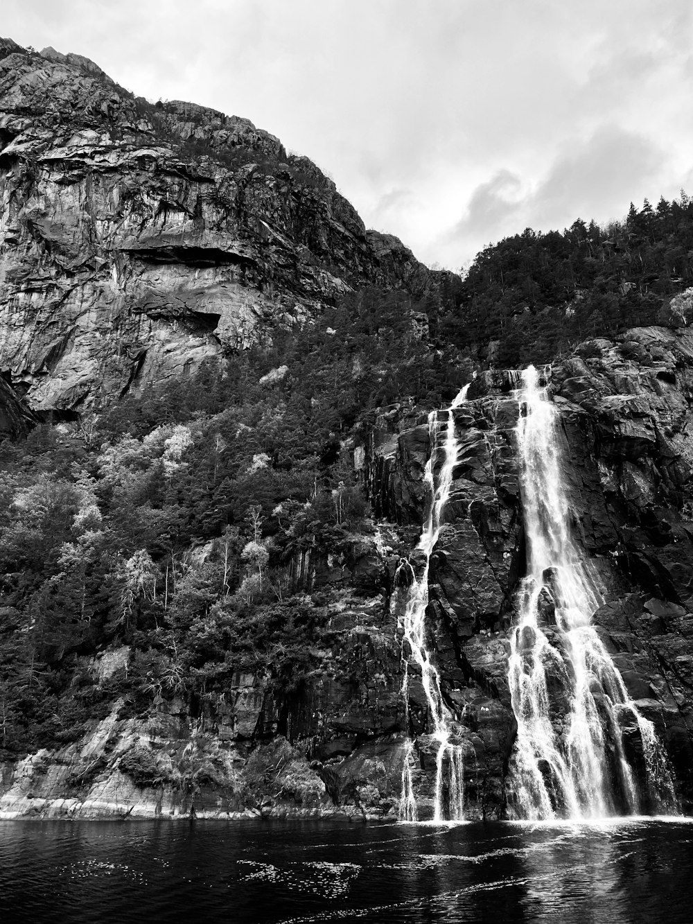 grayscale photo of waterfalls under cloudy sky