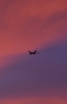 An airplane soaring above clouds during a vibrant sunset.
