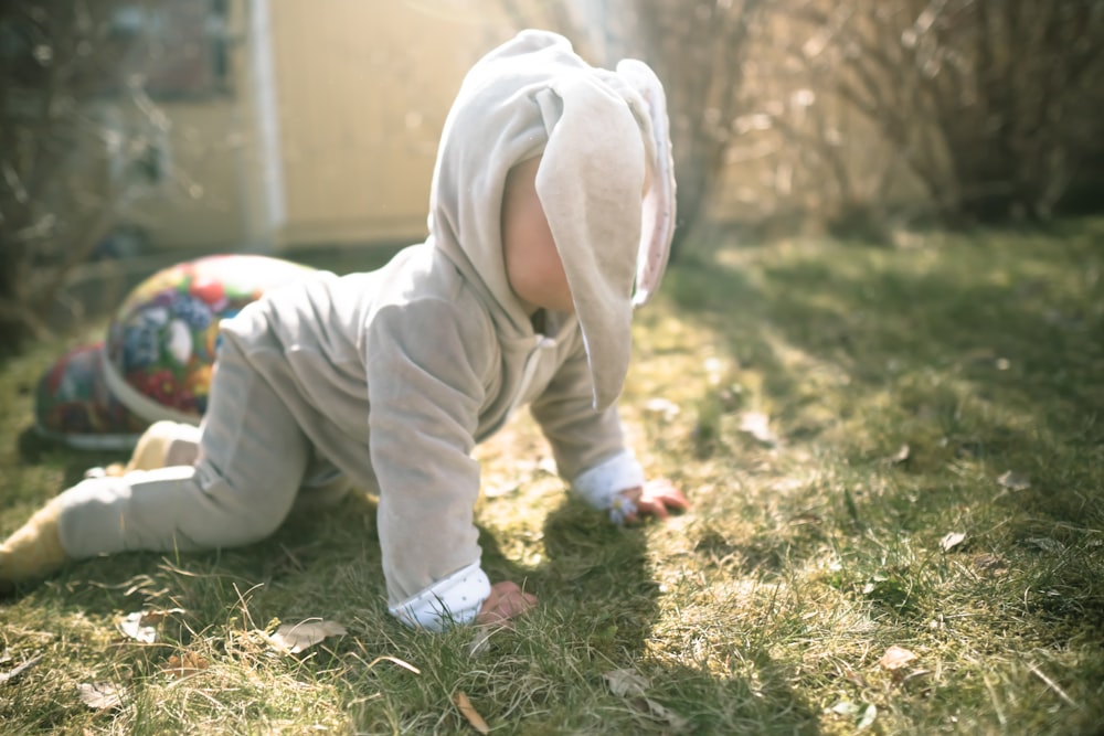 bambino in felpa con cappuccio bianca e pantaloni che si siedono sull'erba verde durante il giorno