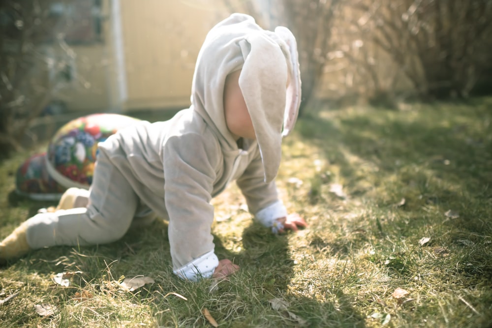 child in white hoodie and pants sitting on green grass during daytime