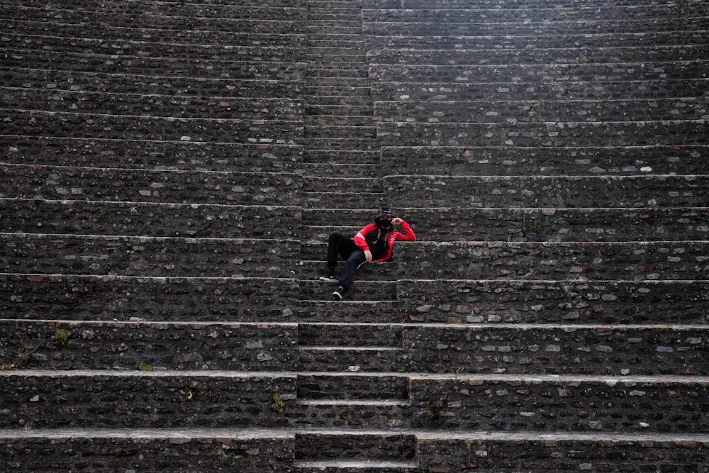 Persona in giacca nera e pantaloni rossi sdraiata su scale di cemento grigio