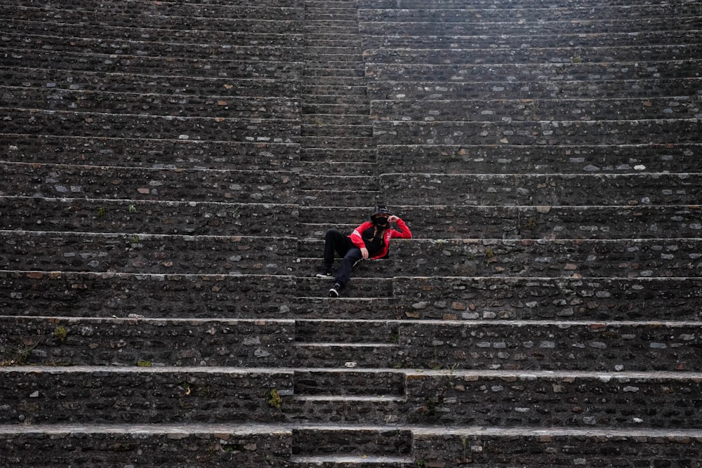 person in black jacket and red pants lying on gray concrete stairs