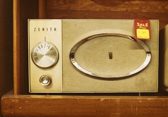 A vintage Zenith radio with a tuning dial and speaker grille, set within a wooden shelf. A 'Sale' tag with a handwritten price is attached to the radio.