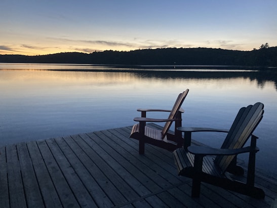 Two wooden chairs on dock overlocking a calm lake with glassy water.