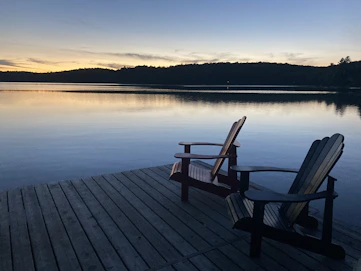Calm lakeside dock in Muskoka with classic Muskoka chairs overlooking still water.