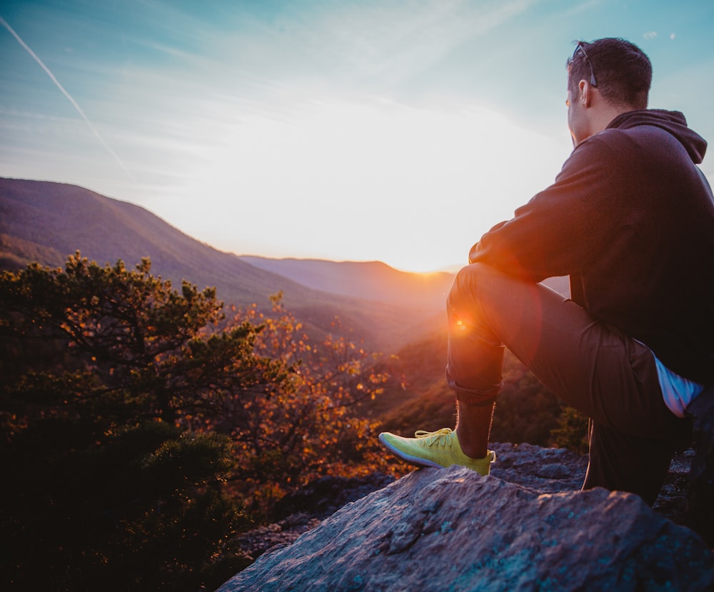 man in black jacket sitting on rock during daytime