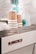 A stack of paper cups with cork sleeves featuring the text 'BREW LAB' is placed on a coffee machine. The brand name 'LA MARZOCCO' is prominently displayed on the machine, which has a sleek design. Clear plastic cups and a turquoise ornament in the background add to the modern aesthetic.