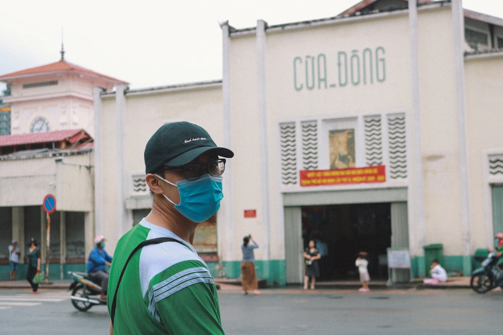 homem em camisa verde e branca vestindo boné preto em pé perto do edifício branco durante o dia