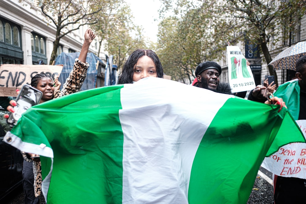 mulher na camisa preta e branca que segura a bandeira branca e verde durante o dia