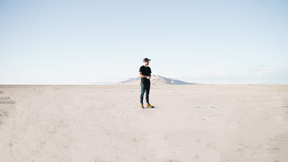 man in black jacket and blue denim jeans walking on brown sand during daytime