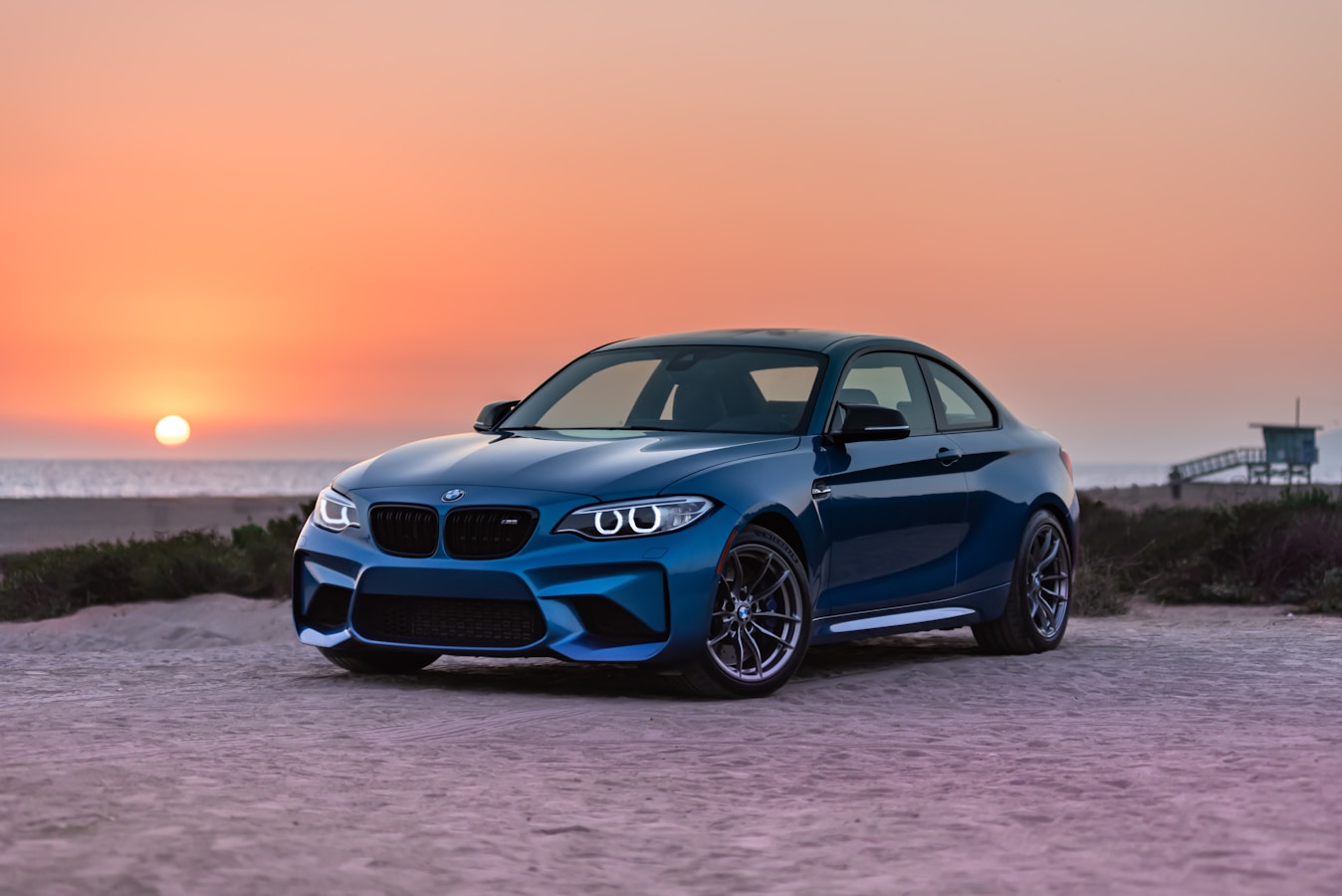 Gleaming blue BMW M2 at sunset on a San Diego beach showcasing professional detailing results