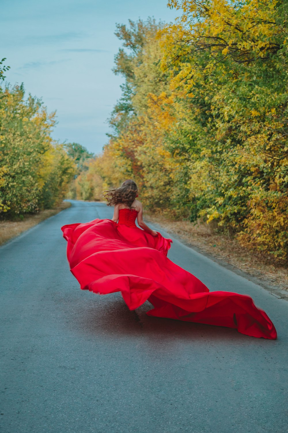 Donna in vestito rosso che si siede sulla strada di cemento grigia durante il giorno